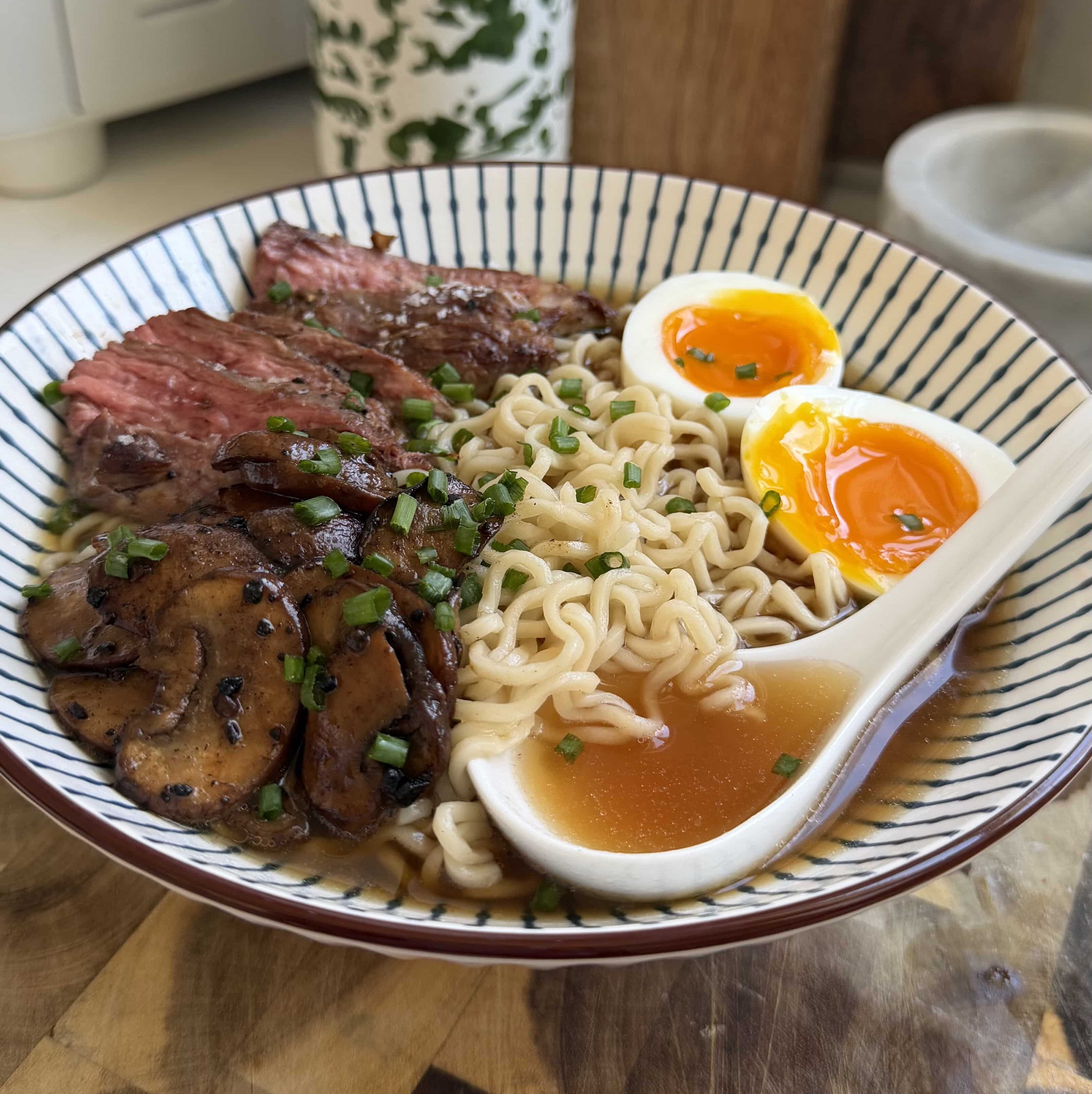 Sliced steak, jammy eggs, ramen noodles, and a spoon in a bowl.