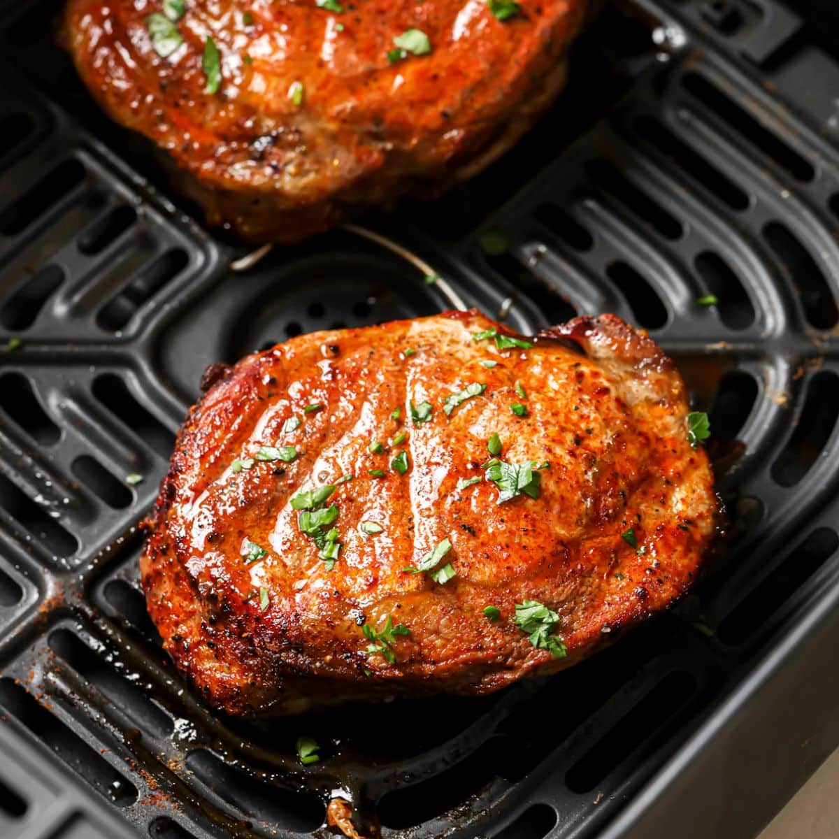 Two air fryer pork chops resting in an air fryer basket after cooking.