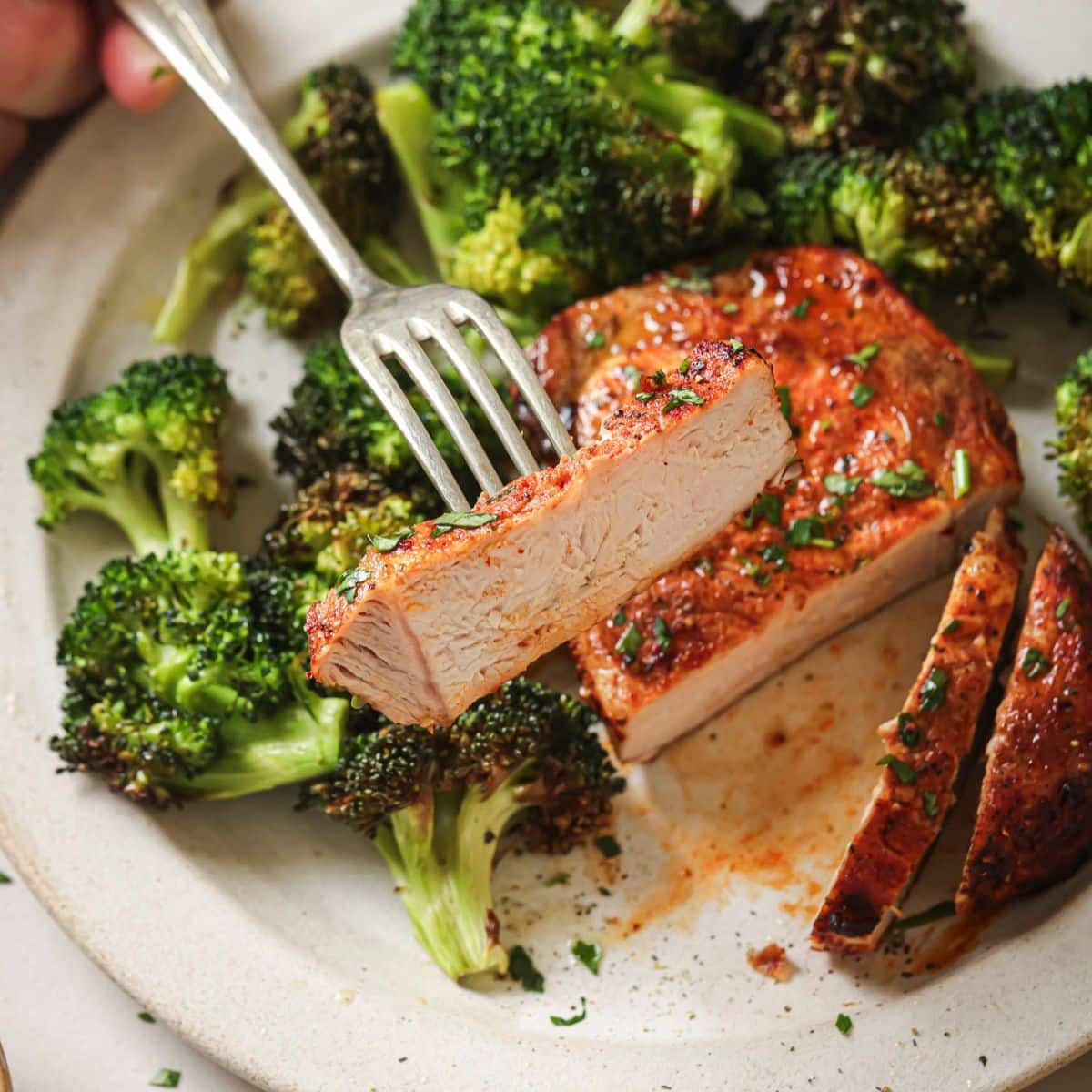 Sliced pork chops on a plate next to broccoli with a fork lifting one piece off of the plate. 