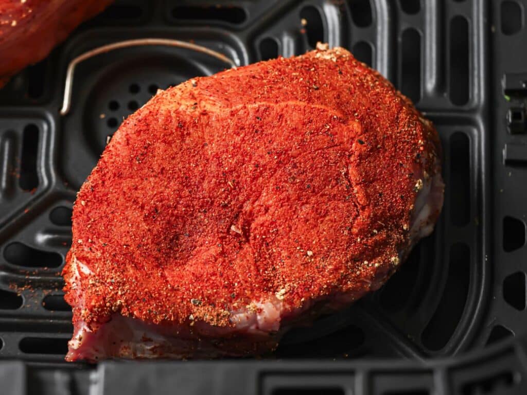 A raw pork chop in the air fryer ready to be cooked. 