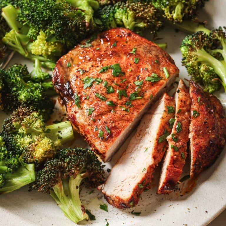 Sliced air fryer pork chops on a white plate next to cooked broccoli.