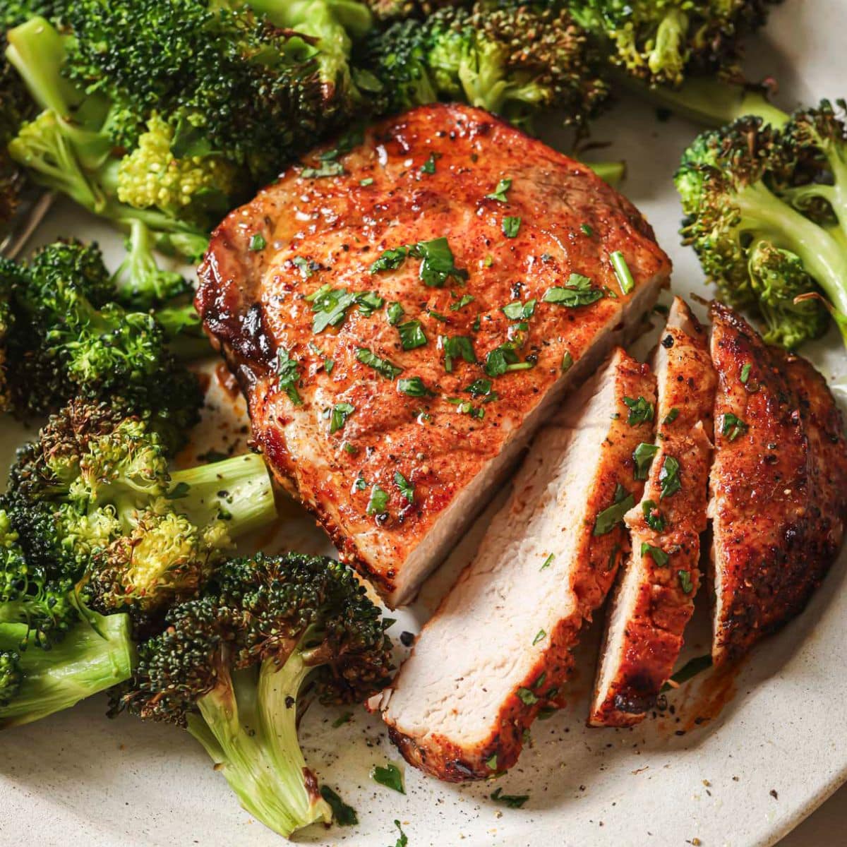 Sliced air fryer pork chops on a white plate next to cooked broccoli.