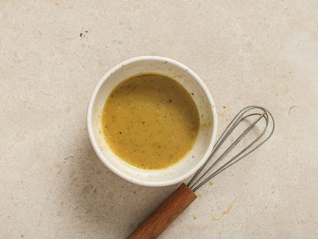 A bowl of the lemon orzo pasta salad dressing ingredients combined with a whisk. 