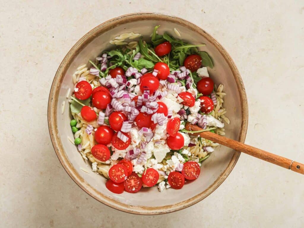 Lemon orzo pasta salad in a bowl topped with tomatoes, onions and feta and combined with the dressing.