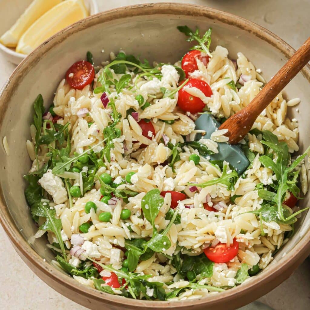 Lemon orzo pasta salad in a bowl with a wooden serving spoon.