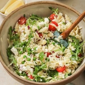 Lemon orzo pasta salad in a bowl with a wooden serving spoon.