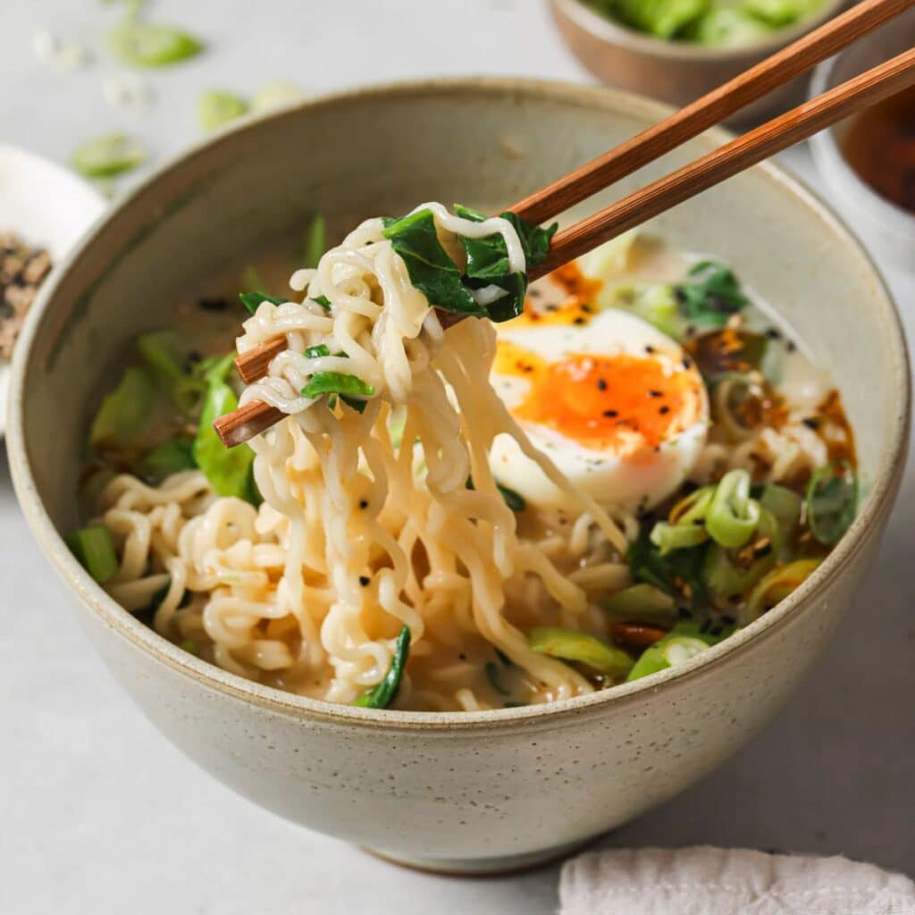 chopsticks picking up spicy ramen noodles out of a bowl