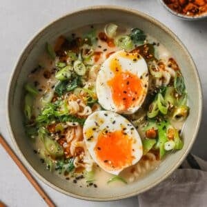 a bowl of spicy ramen topped with jammy eggs, sesame seeds, and furikake seasoning.