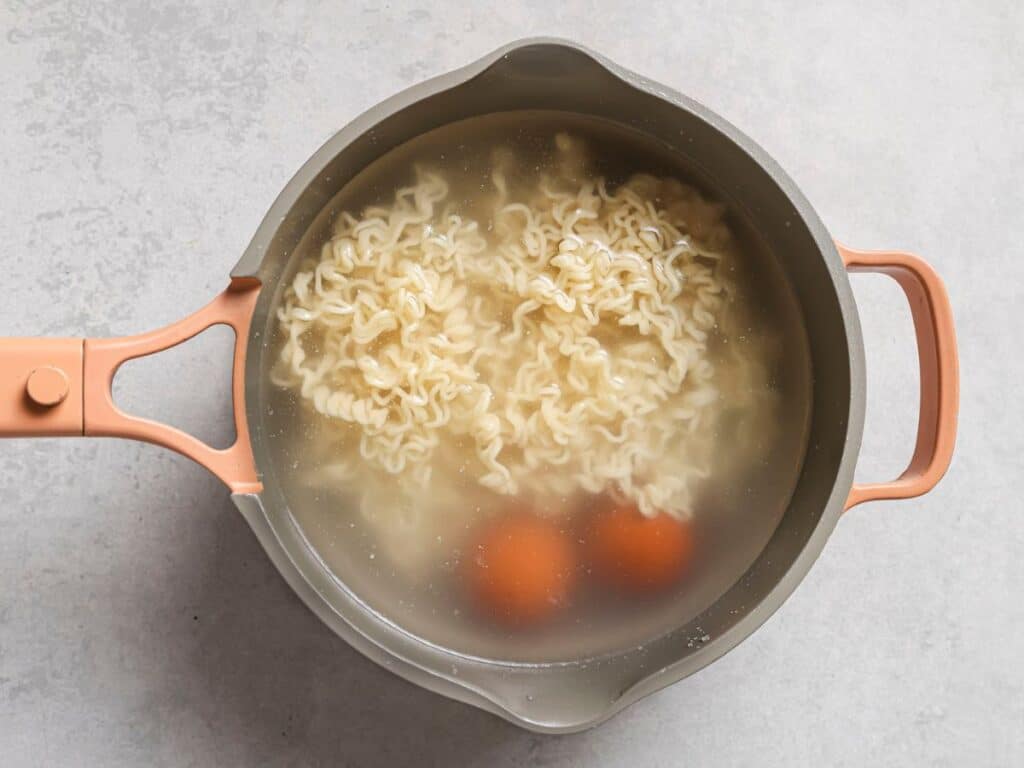 adding the ramen to the pot with the eggs