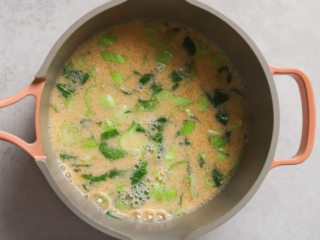 warming the spicy ramen broth and bok choy in a saucepan