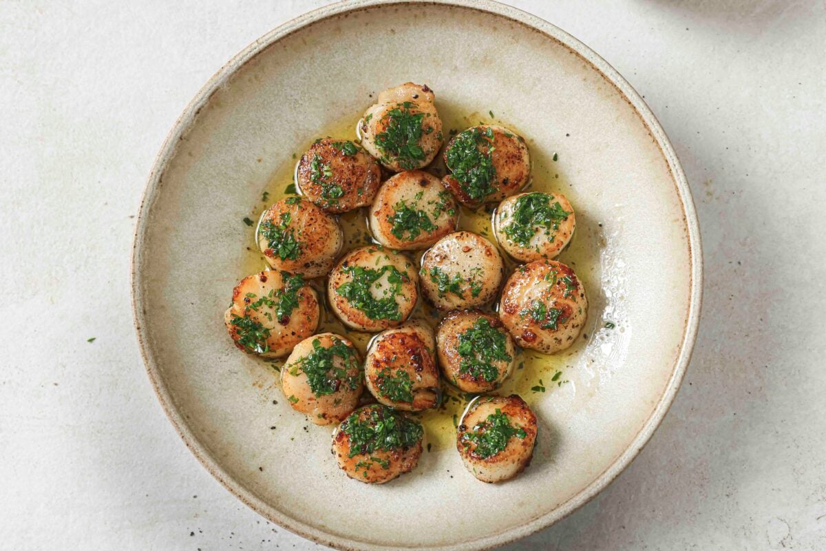 Pan-seared scallops finished with parsley butter in a bowl on a white countertop.