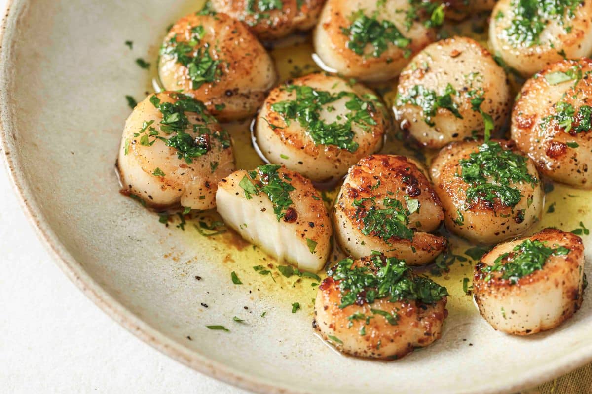 Finished scallops on a plate with parsley butter on top.