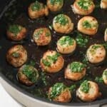 Pan-seared scallops topped with parsley butter in a black pan.