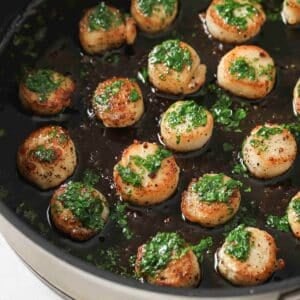Pan-seared scallops topped with parsley butter in a black pan.