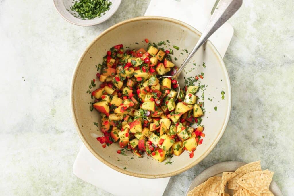 A bowl of fresh peach salsa made with juicy peaches, red bell pepper, jalapeño, and cilantro.