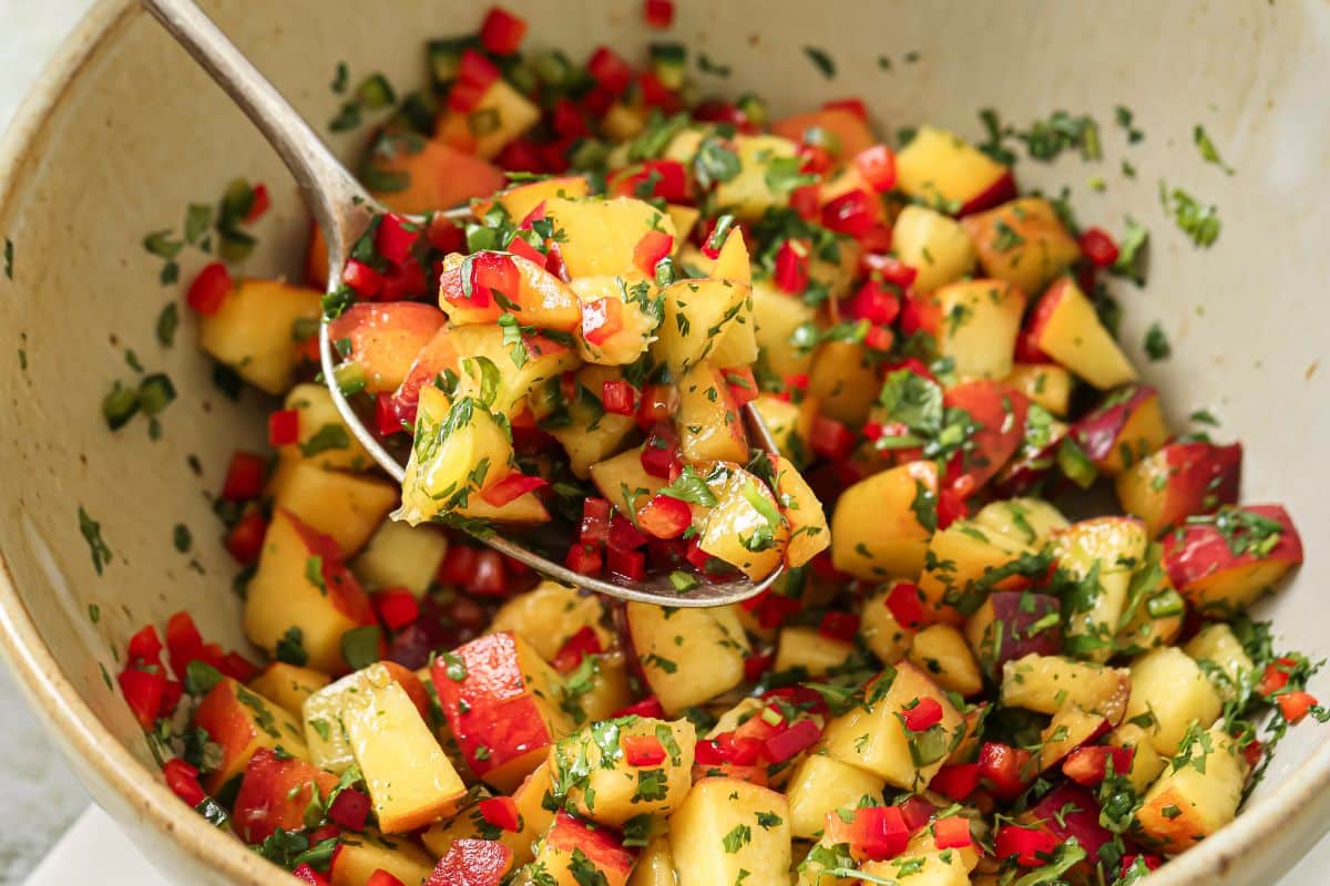 a spoon holding up a bite of fresh peach salsa to show the chunky texture.