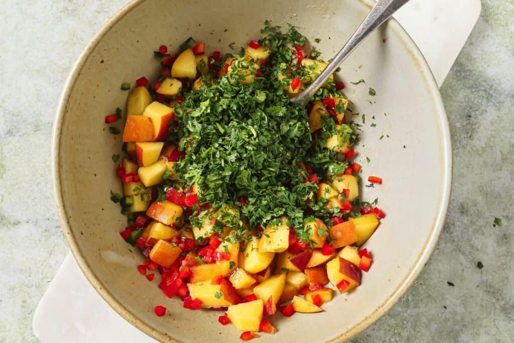 Adding chopped cilantro to the mixing bowl with the rest of the peach salsa ingredients.
