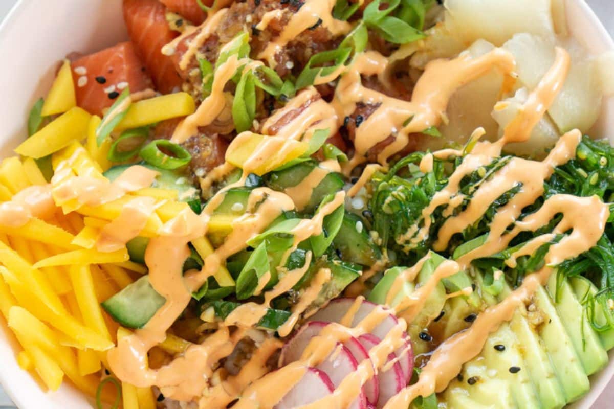 A close up salmon poke bowl drizzled with spicy mayo.