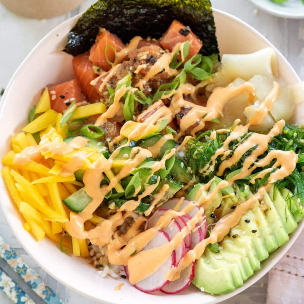 A salmon poke bowl drizzled with spicy mayo in a white bowl. 