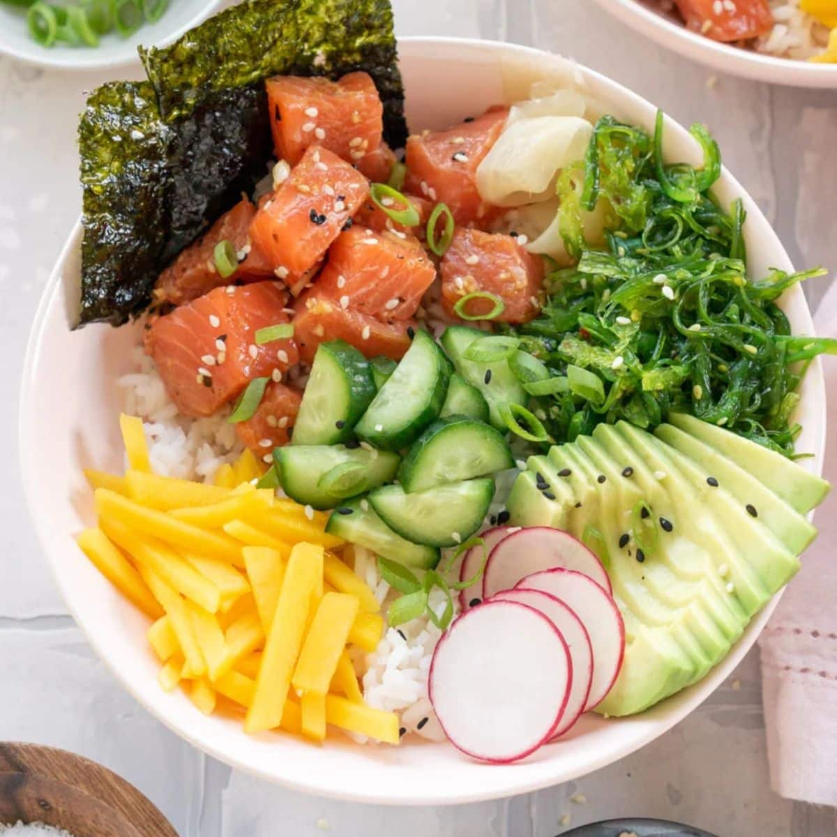 Close up of a salmon poke bowl with avocado, mango, radish, and seaweed salad.
