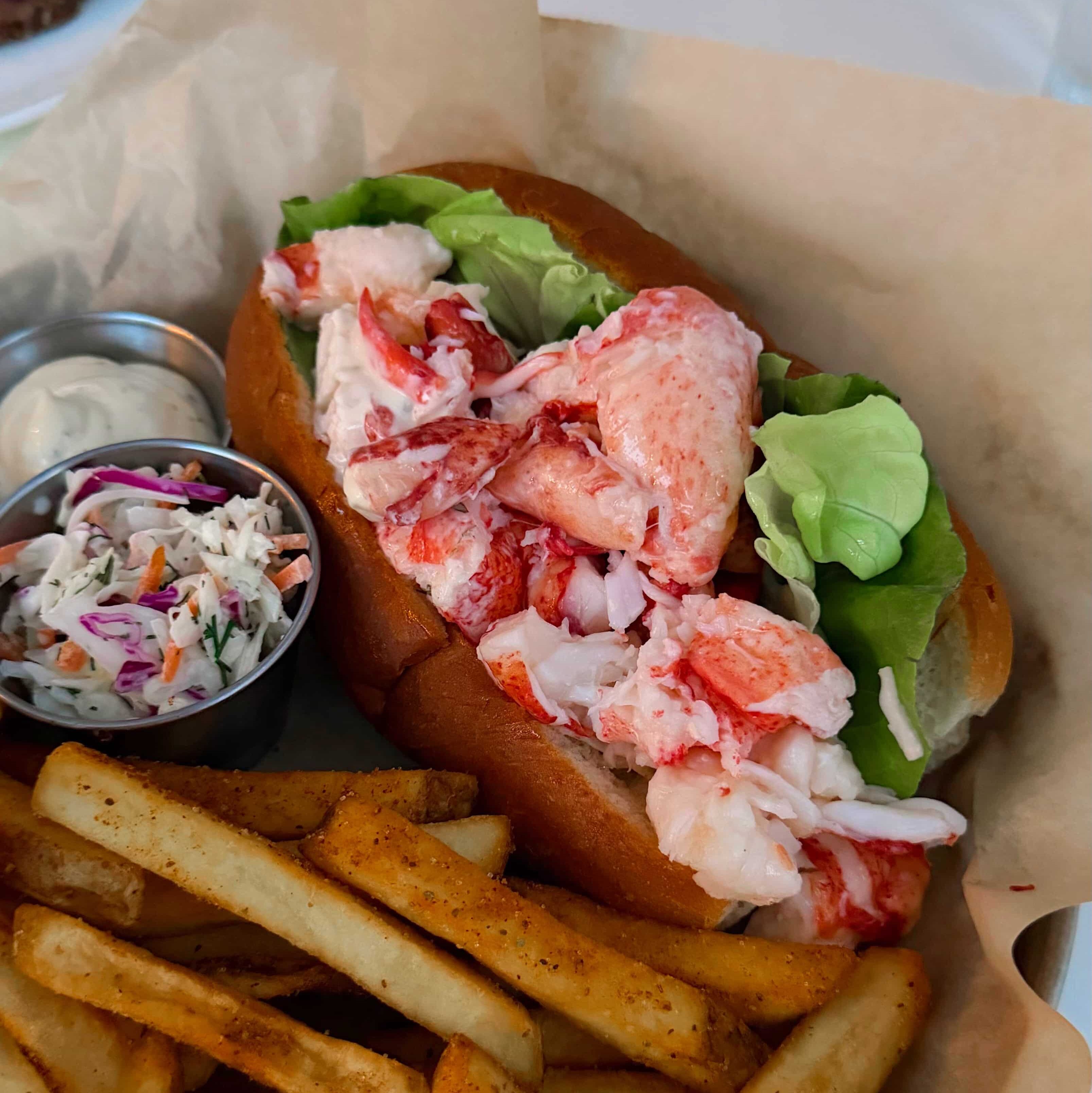A lobster roll with french fries and coleslaw on the side.