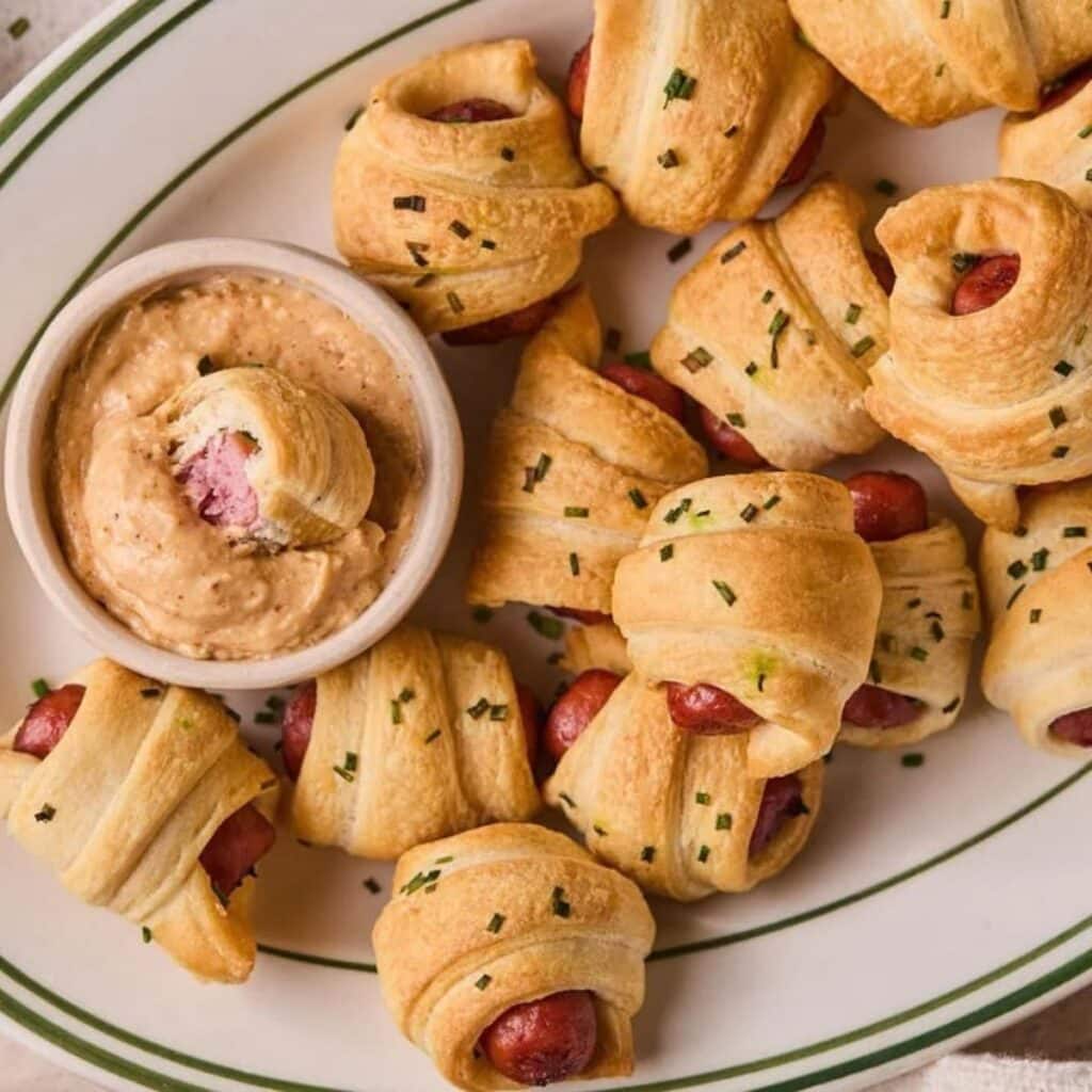 A plate full of air fryer pigs in a blanket with a side of homemade queso dip.