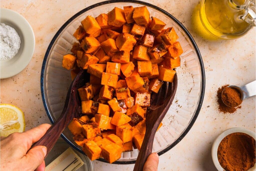 Tossing raw sweet potatoes with honey butter before spreading them onto the baking sheet. 