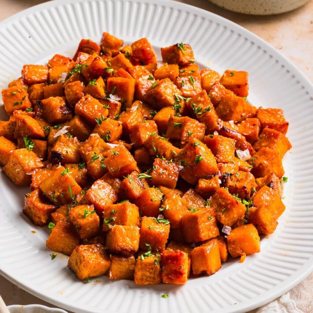 Honey roasted sweet potatoes on a white platter with crispy caramelized edges and flaky sea salt on top.