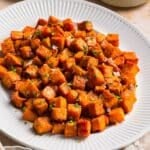 Honey roasted sweet potatoes on a white platter with crispy caramelized edges and flaky sea salt on top.