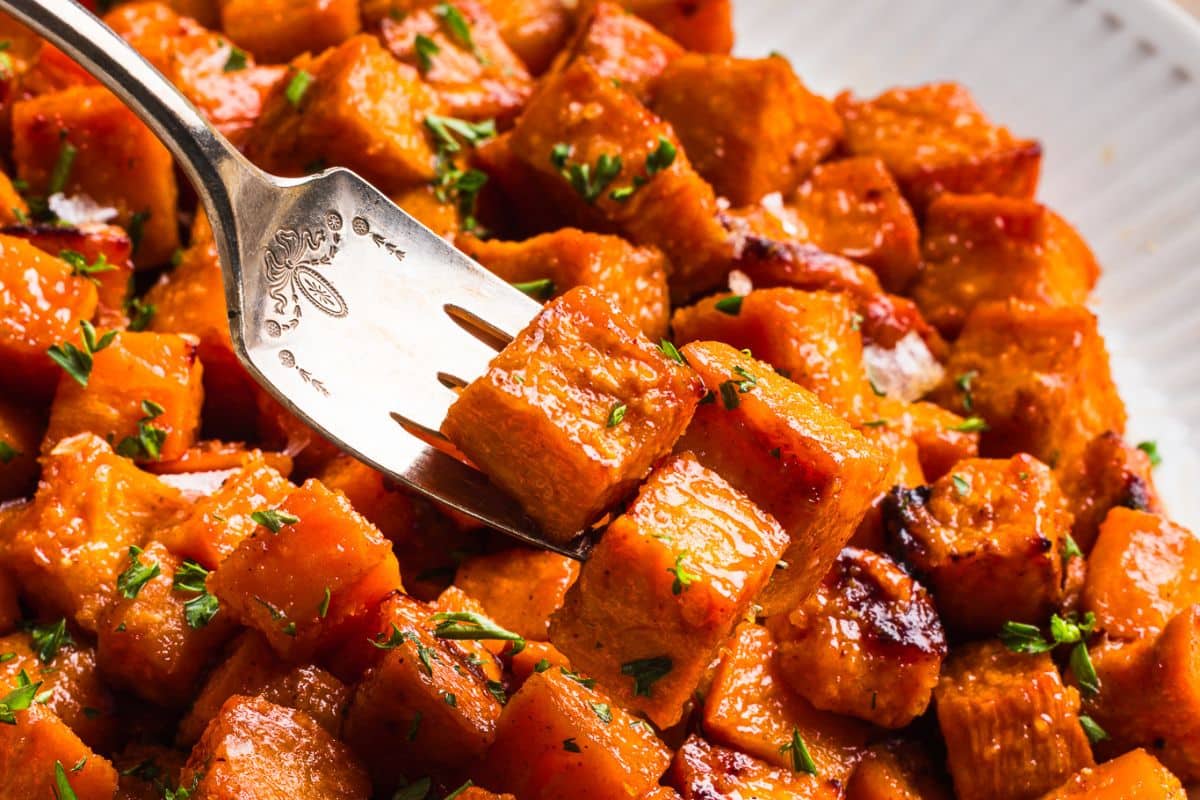 A fork piercing a piece of honey roasted sweet potatoes out of a larger dish. 