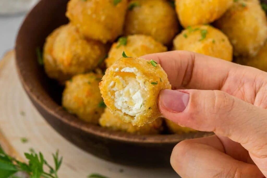 A hand holding a goat cheese ball with a bite taken out to show the middle. 