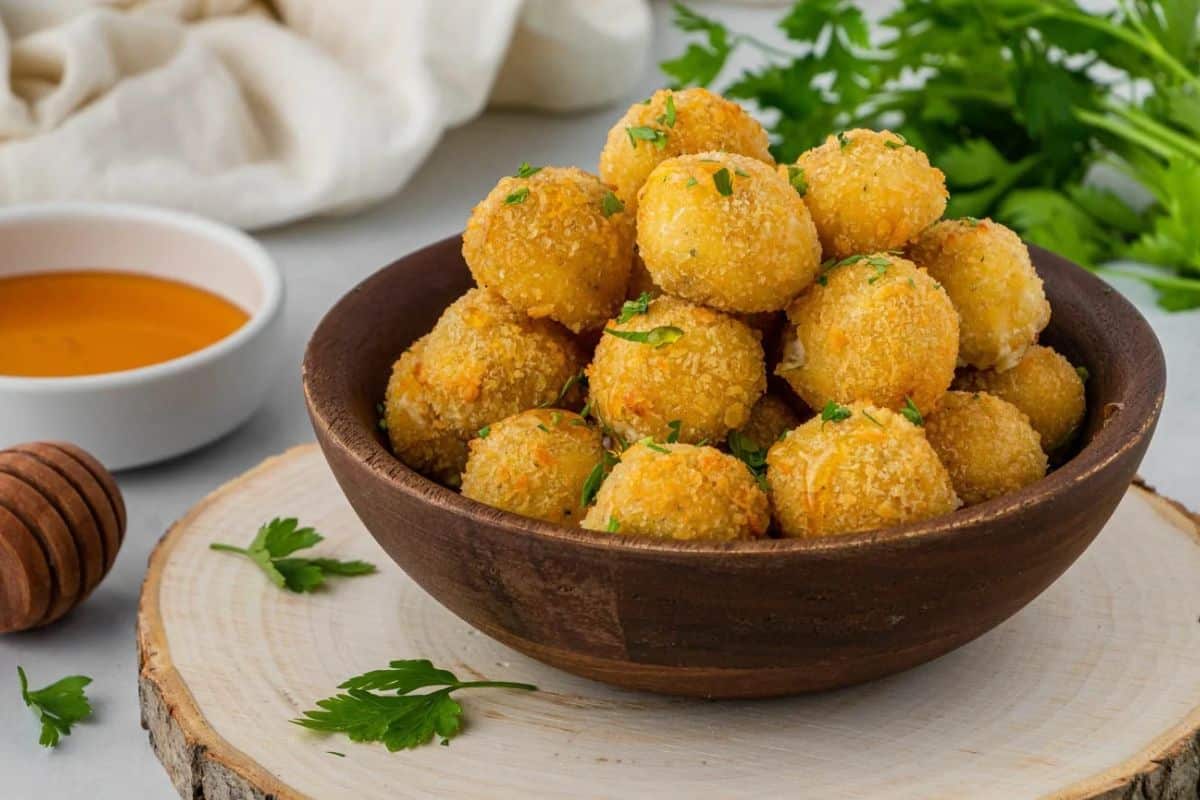 A brown bowl of air fryer cheese bites on a wooden serving platter.